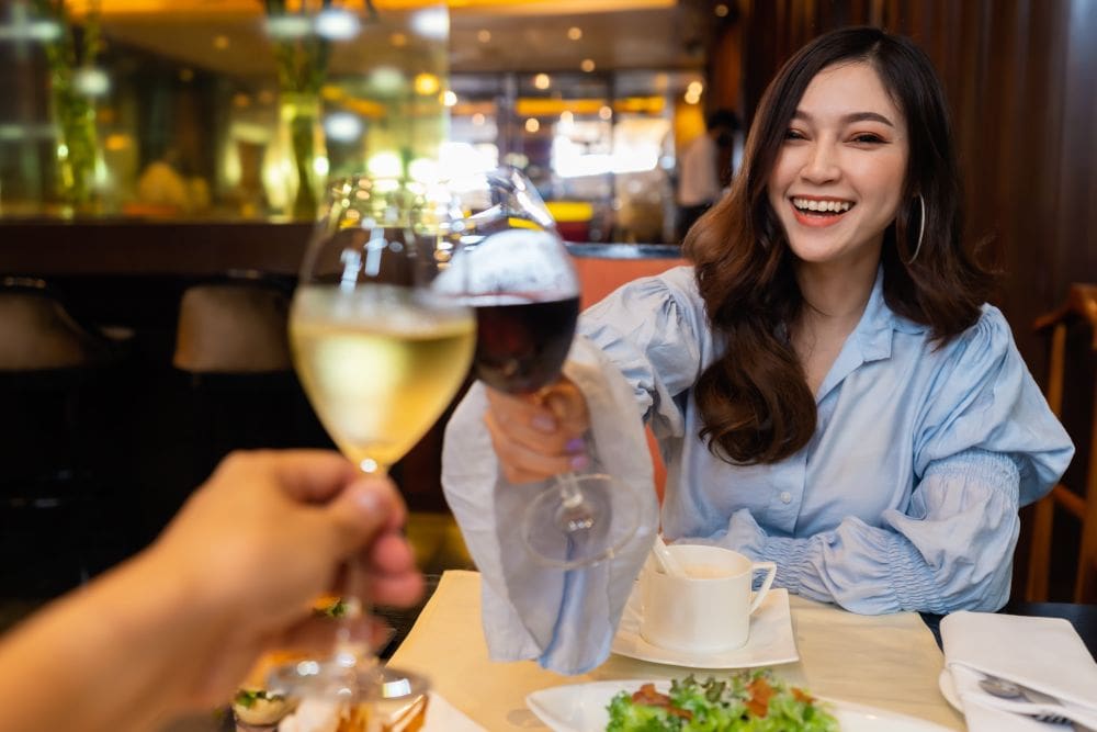 A woman enjoying red wine with Thai food, while a man chooses white wine.