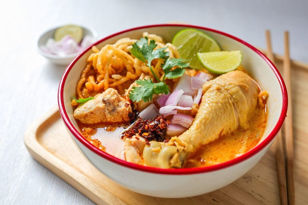 ข้าวซอยไก่สูตรต้นตำรับ พร้อมเส้นทอดกรอบ หอมแดง มะนาว และพริกน้ำมัน